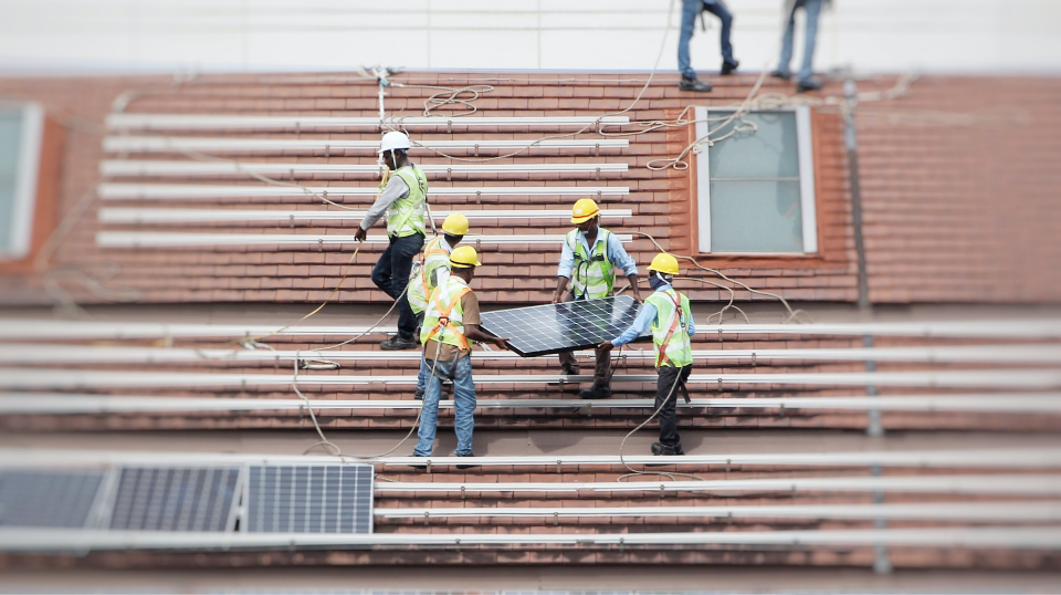 engenheiros carregando placa solar em cima de um telhado